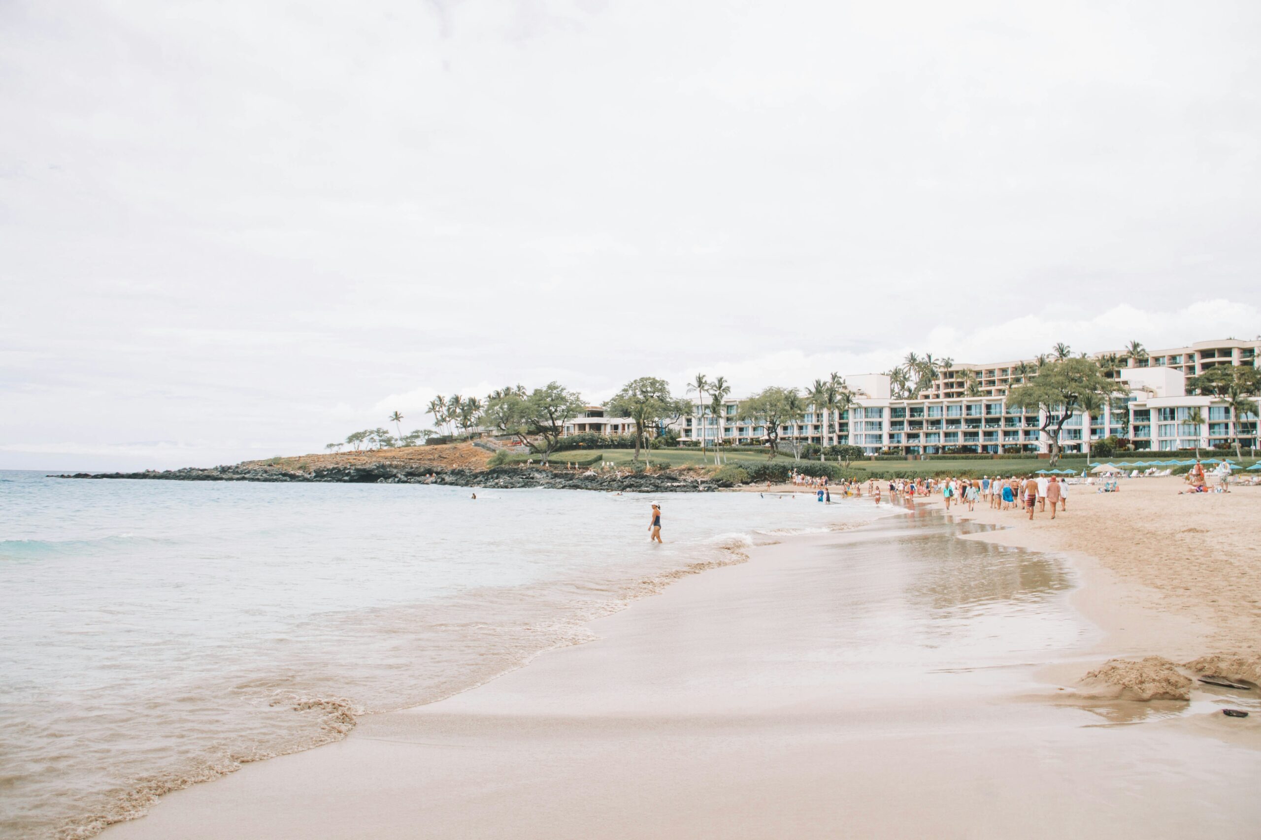 Low-rise beachfront resort buildings along a wide sandy bay in Hawaii