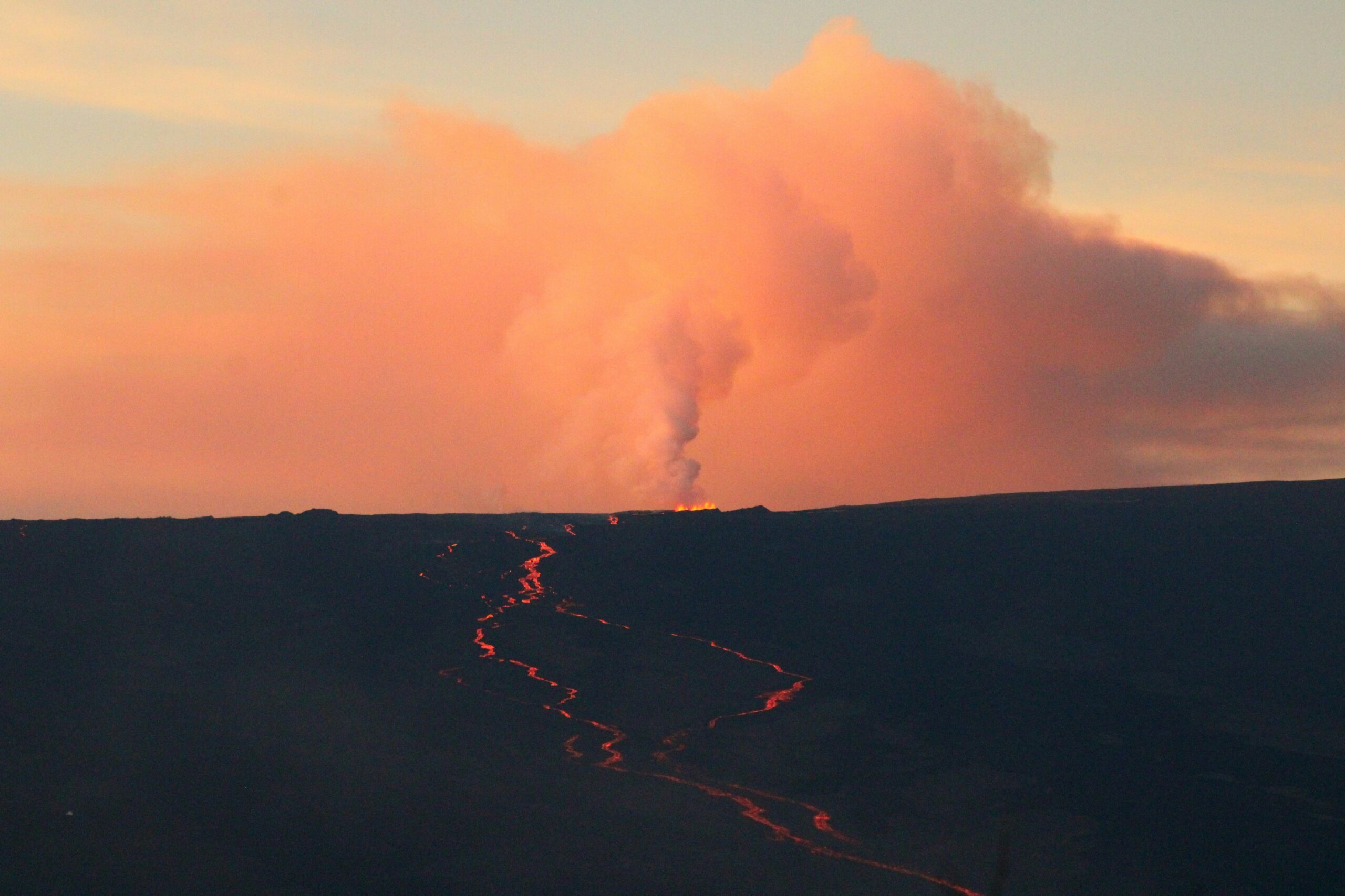 Glowing lava flow and a tall steam plume at sunset on the Big Island