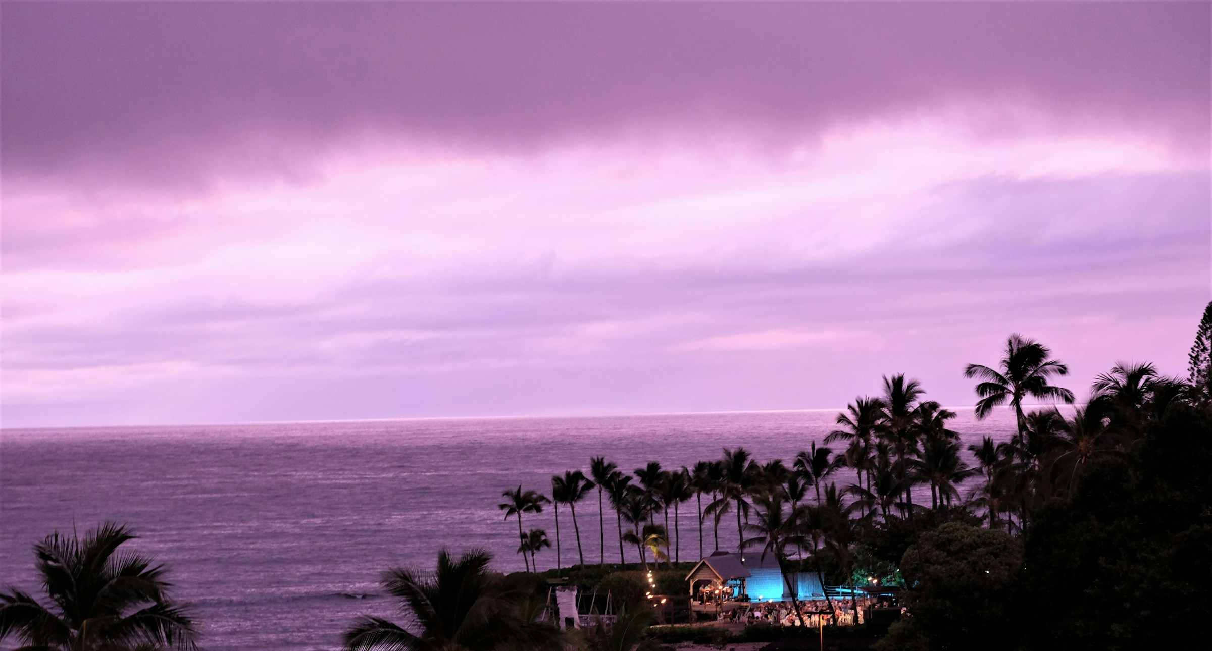 Oceanfront resort lit up at dusk beneath palm trees on the Kona coast